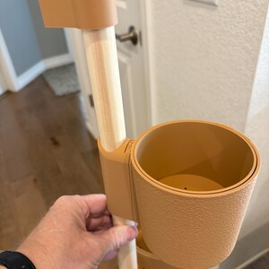 Puede incluir: Un soporte para plantas de varios niveles de color beige con un poste de madera clara. El soporte tiene dos portavasos y una pieza superior. El soporte est&aacute; dise&ntilde;ado para sostener plantas y otros art&iacute;culos.