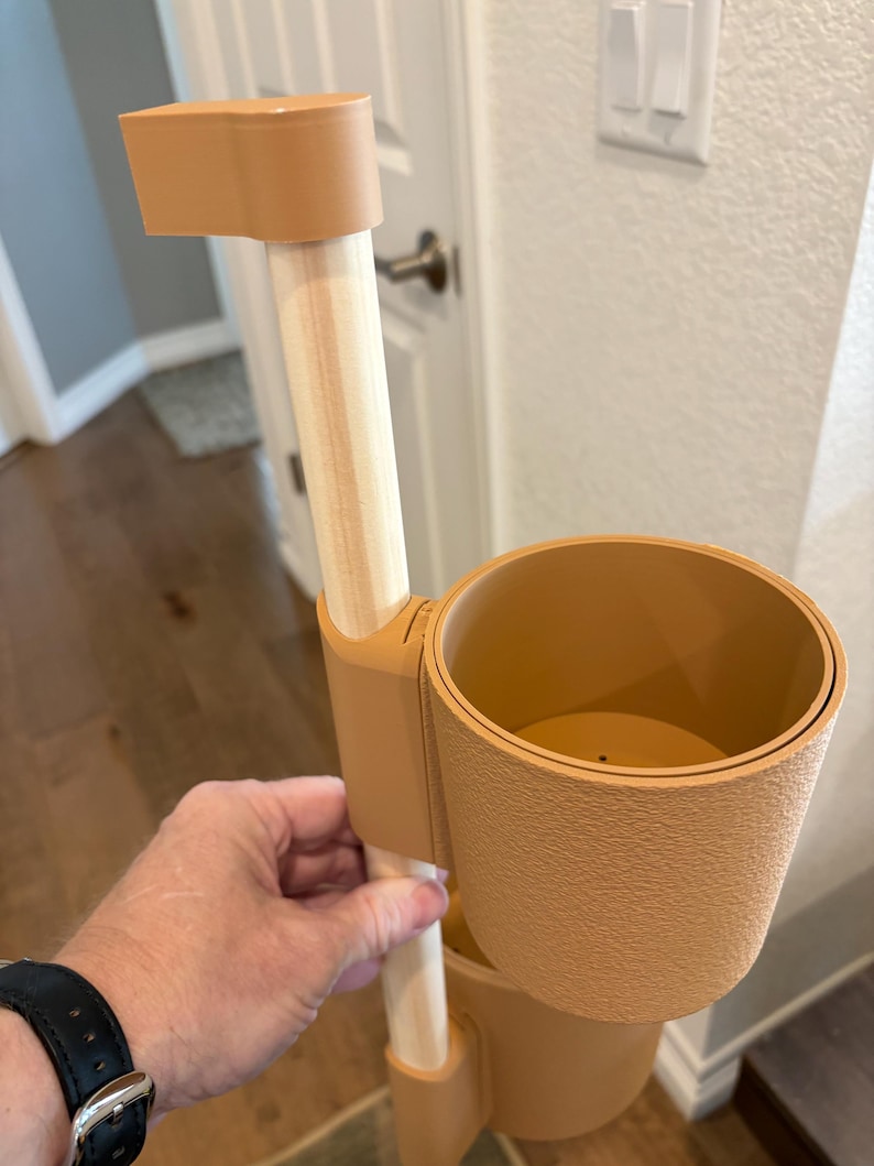 Puede incluir: Un soporte para plantas de varios niveles de color beige con un poste de madera clara. El soporte tiene dos portavasos y una pieza superior. El soporte est&aacute; dise&ntilde;ado para sostener plantas y otros art&iacute;culos.