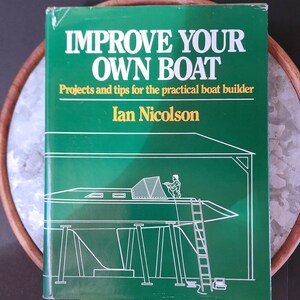 May include: Green book cover with the title "Improve Your Own Boat" and the subtitle "Projects and tips for the practical boat builder" by Ian Nicolson. The cover features a line drawing of a boat on supports with a person working on it.