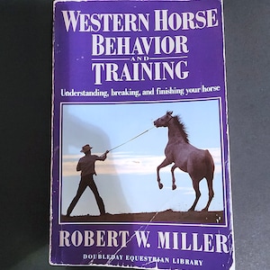 May include: A purple book titled "Western Horse Behavior and Training" with a photo of a horse being led by a person on the cover. The book is part of the Doubleday Equestrian Library.