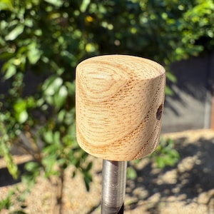 May include: A wooden mallet with a light brown, cylindrical head and a silver metal handle. The head has visible wood grain and a small hole. The tool is designed for striking or shaping materials.