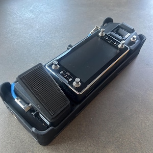May include: Black effects pedal with a rectangular screen and silver knobs. A black foot pedal is connected to the main unit with a blue cable. The device is designed for use with musical instruments.