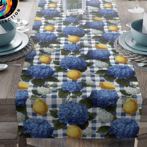 May include: A table runner with a blue and white checkered pattern, adorned with blue hydrangea flowers and yellow lemons. The runner is made of polyester and is displayed on a wooden table. The text "Hydrangea & Lemons Table Runner" is visible.