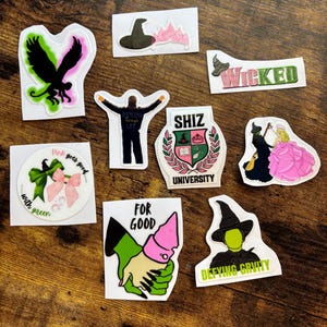 Może przedstawiać: Kolekcja kolorowych naklejek z wzorami i tekstami z musicalu "Wicked". Naklejki zawierają obrazy kapelusza czarownicy, czarnego ptaka oraz słowa "Wicked", "For Good" i "Defying Gravity".