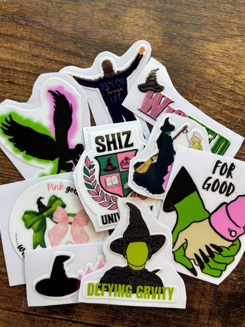 Może przedstawiać: Kolekcja kolorowych naklejek z obrazami i tekstem z musicalu "Wicked". Projekty obejmują sylwetki, kapelusze czarownic i frazy takie jak "Defying Gravity" i "For Good".