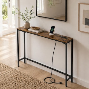 Pode incluir: Uma consola longa e estreita com um tampo castanho com efeito de madeira e uma estrutura de metal preta. A mesa tem uma estação de carregamento integrada e é decorada com um vaso de vegetação, uma tigela e livros. Um smartphone está a carregar na mesa.