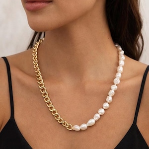 May include: A gold chain necklace with a section of white baroque pearls. The necklace is worn around the neck and is a mix of classic and modern styles. The chain is a curb link design.