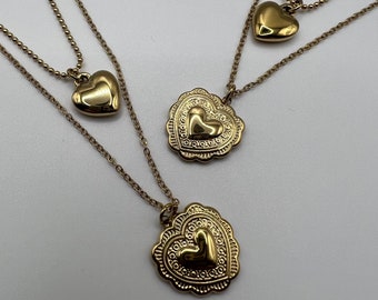 May include: Three gold necklaces with heart-shaped pendants. The pendants are different sizes and have intricate designs.