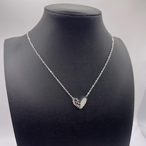 以下が含まれることがあります： 銀色のチェーンネックレスにハート型のペンダントがついたもの。ペンダントは半分が白、半分が黒の2つの部分で構成されています。