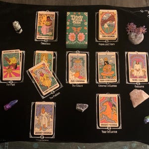 May include: A black tarot cloth with several tarot cards and crystals. The cards are in clear plastic sleeves and feature colorful illustrations and text. The deck box reads "Flower Child Tarot". The cards include "Conscious", "Ten-Wands", "The Past", "Ace-Swords", "Four-Pentacles", "Nine-Cups", "Queen-Swords", and "Knight-Wands".