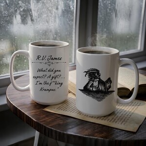 Puede incluir: Dos tazas de cer&aacute;mica blanca con dise&ntilde;os en tinta negra. Una taza presenta el texto R.V. James seguido de What did you expect? A gift?... I'm the f**king Krampus. La otra taza muestra una ilustraci&oacute;n de l&iacute;nea negra de un Krampus con cuernos leyendo un libro.