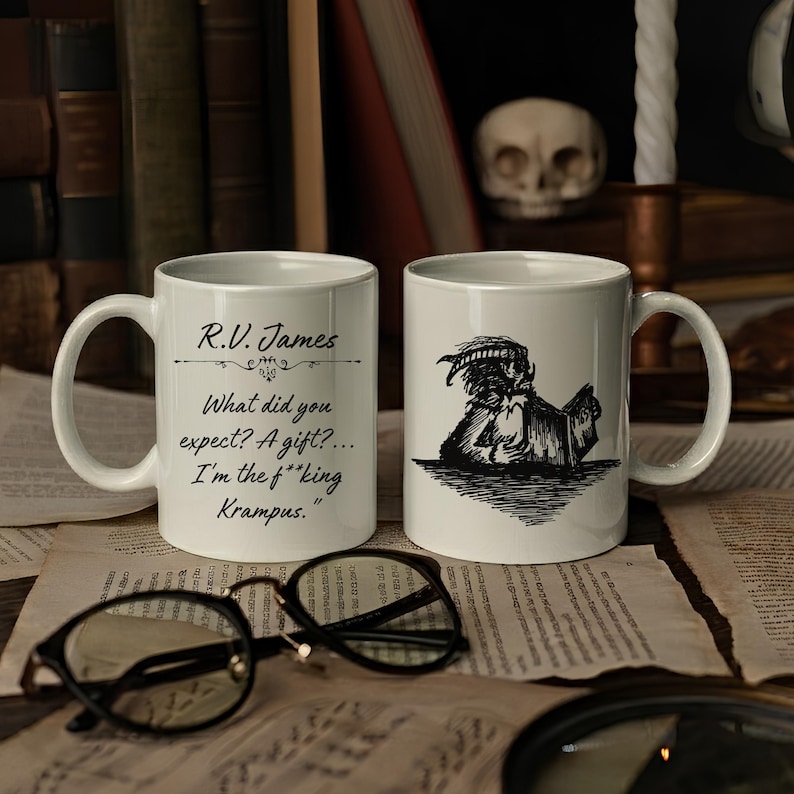 Puede incluir: Dos tazas de cer&aacute;mica blanca con dise&ntilde;os en tinta negra. Una taza muestra el texto: R.V. James, What did you expect? A gift?... I'm the f**king Krampus. La otra taza presenta una ilustraci&oacute;n en tinta negra de una criatura con cuernos leyendo.