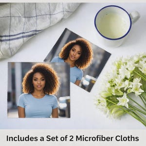 Pode incluir: Dois panos de microfibra com um retrato de mulher, uma caneca branca com borda azul e um buquê de flores brancas são dispostos sobre uma superfície branca. O texto diz: "Inclui um conjunto de 2 panos de microfibra."