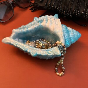 May include: A light blue seashell trinket dish with a pearl necklace and other jewelry inside.