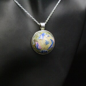 May include: A silver chain necklace with a round pendant featuring a colorful floral design. The pendant is made of glass and has a white background with blue, pink, and green flowers.