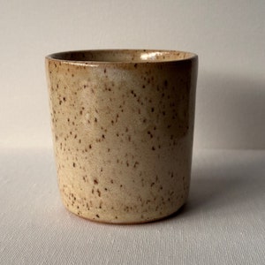 May include: A speckled beige ceramic planter with a rounded bottom and a slightly flared top.