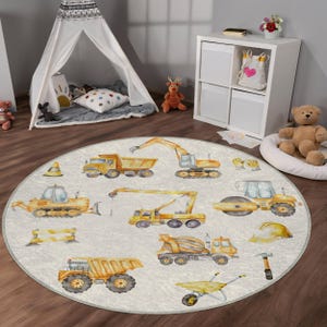 May include: A round, white play rug with a construction theme. The rug features yellow construction vehicles, tools, and a hard hat. The vehicles include a bulldozer, a crane, a dump truck, a cement mixer, and a steamroller.
