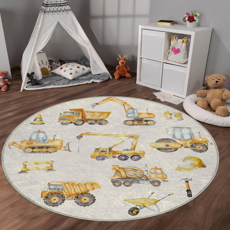 May include: A round, white play rug with a construction theme. The rug features yellow construction vehicles, tools, and a hard hat. The vehicles include a bulldozer, a crane, a dump truck, a cement mixer, and a steamroller.