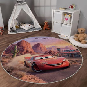 Può includere: Tappeto rotondo con un paesaggio desertico con un'auto da corsa rossa, Saetta McQueen, che corre su una strada. Il tappeto ha il nome "William" stampato sopra. Lo sfondo include un ristorante Route 66 e un tramonto.