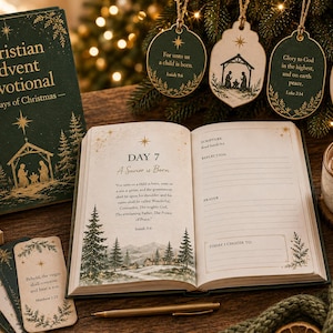 May include: A dark green Christian Advent Devotional book with gold foil text and a nativity scene. An open book displays Day 7, A Savior is Born, with scripture and writing prompts. Four hanging wooden ornaments and a mug of hot cocoa are present.