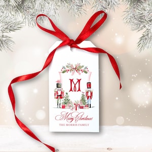 May include: White gift tag with a red ribbon, featuring a watercolor design of nutcrackers, Christmas trees, and gifts. The tag includes the text "Merry Christmas" and a family name.