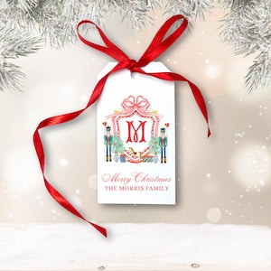 May include: A white Christmas gift tag tied with a red ribbon. The tag displays a red initial "M" within a decorative frame, with toy soldiers and Christmas trees. The text "Merry Christmas" and "THE MORRIS FAMILY" are printed below.