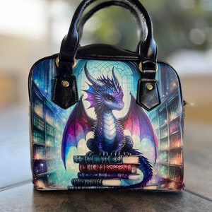 May include: A square handbag with a fantasy theme. The bag features a blue and purple dragon sitting on a stack of books in front of a library backdrop. The bag has black handles and gold-colored hardware.