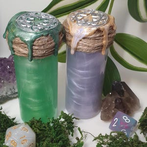 Könnte beinhalten: Zwei kleine Glasflaschen mit dekorativen Deckeln und einer schimmernden, irisierenden Flüssigkeit im Inneren. Die Deckel sind aus Metall und haben ein Sternmuster. Die Flaschen sind mit Schnur umwickelt und haben einen tropfenden Wachsstempel.