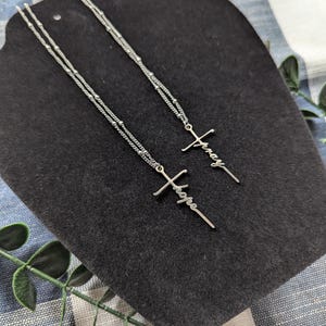 May include: Two silver necklaces with cross pendants. The pendants are inscribed with the words "pray" and "hope".
