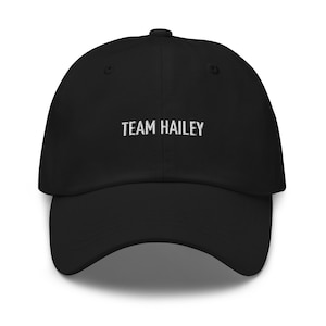 May include: Black baseball cap with white embroidered text that reads "TEAM HAILEY".