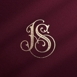 May include: A metallic gold monogram featuring the intertwined letters J and S in a decorative, calligraphic script font. The letters are centered against a solid, deep burgundy background with a subtle, fine-grained texture throughout.