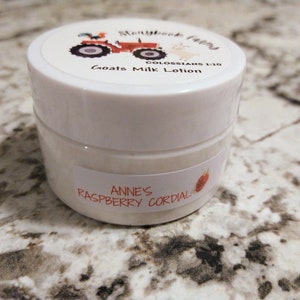 May include: A white jar of goat's milk lotion with a label that reads "Storybook Farms" and "Goats Milk Lotion." The jar also has a label that says "Anne's Raspberry Cordial."