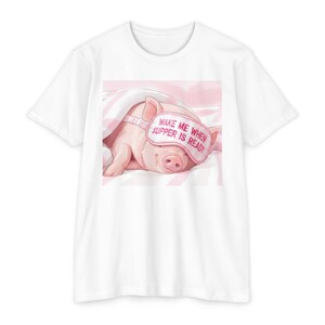 May include: White t-shirt featuring a graphic of a sleeping pig wearing a pink eye mask. The eye mask has the text "WAKE ME WHEN SUPPER IS READY". The pig is under a pink blanket.