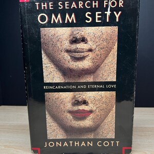 May include: A hardcover book titled "The Search for Omm Sety" by Jonathan Cott. The cover features a black background with the title in white and two stone-like faces. The subtitle reads "Reincarnation and Eternal Love."