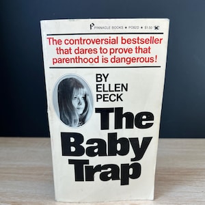 May include: A vintage paperback book titled "The Baby Trap" by Ellen Peck. The cover features a black and white portrait of a woman and bold white text on a cream background. The book's tagline reads, "The controversial bestseller that dares to prove that parenthood is dangerous!"