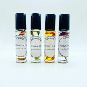 May include: Four glass roller bottles with black caps and labels. The labels feature floral designs and text that reads "POTIONS & SUCH" and "From Nature with Love". The bottles contain different coloured liquids and dried flowers. The scents are Peach Cobbler, Sweet Cucumber Melon, Wild Orange, and Vanilla Rose.