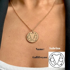 May include: A gold necklace with a round pendant featuring a Gallifreyan symbol. The pendant is engraved with a circular design and the text "Sabrina".