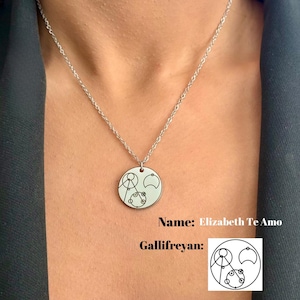 May include: A silver necklace with a round pendant featuring a white Gallifreyan symbol. The pendant has a black outline and the text "Name: Elizabeth Te Amo" and "Gallifreyan:" is printed below the pendant.