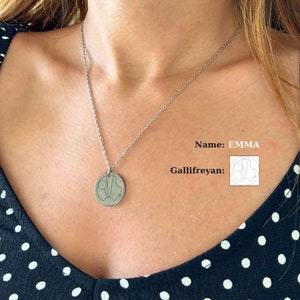 May include: A silver necklace with a round pendant featuring a Gallifreyan symbol. The pendant is engraved with the name "EMMA".