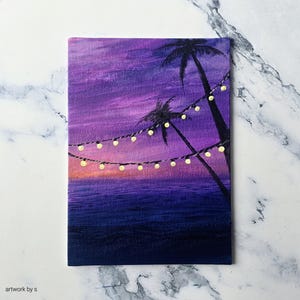 May include: A small canvas painting of a tropical sunset. The artwork shows a purple and orange sky, a dark blue ocean, and silhouetted palm trees. A string of yellow lights hangs across the scene, adding a warm glow. The text "artwork by s" is in the bottom left corner.