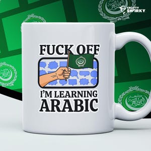 Puede incluir: Taza de cerámica blanca con el texto "FUCK OFF I'M LEARNING ARABIC". La taza presenta una mano de dibujos animados sosteniendo una bandera verde con texto árabe. La taza tiene un asa blanca y está sobre un fondo verde.