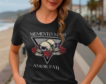 May include: Black t-shirt featuring a graphic design with two skulls, red roses, and the phrases "MEMENTO MORI" and "AMOR FATI" in white. The design is set within a gray triangle. The shirt has a crew neck.