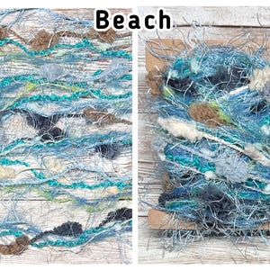 May include: Close-up of two skeins of yarn with a beach theme. The yarn is a mix of blues, greens, and neutral colours, with a textured, fluffy appearance. The word "Beach" is written in black text at the top.