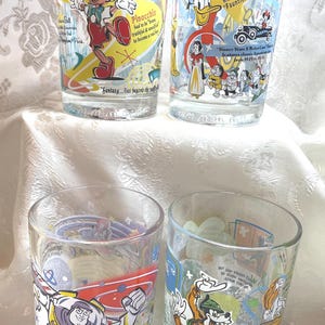 May include: Four clear glass tumblers featuring colorful Disney character graphics and printed text. The glasses display illustrations of Pinocchio, Donald Duck, Snow White, Buzz Lightyear, and Goofy, along with various trivia facts and movie quotes.