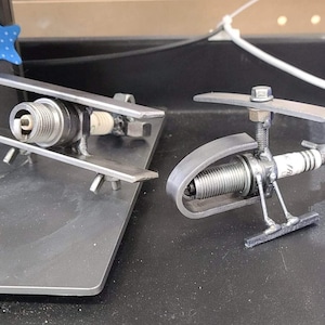 May include: Two small metal sculptures made from spark plugs. One is shaped like a biplane and the other is shaped like a helicopter.