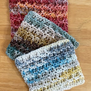May include: Three crocheted dishcloths in a variety of colors, including red, orange, yellow, green, blue, and brown. The dishcloths are stacked on top of each other, with the top dishcloth being a light blue and white color. The dishcloths are labeled "Craft Sale" and "Best Seller!"