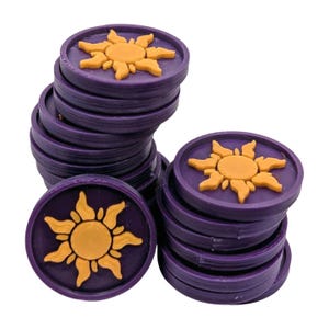 Puede incluir: Un mont&oacute;n de fichas de juego circulares moradas con un dise&ntilde;o de sol amarillo en relieve en el centro. Las fichas est&aacute;n apiladas en varias pilas, con algunas fichas visibles en primer plano. El dise&ntilde;o del sol tiene m&uacute;ltiples rayos.