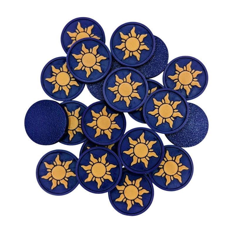 Puede incluir: Una colecci&oacute;n de fichas circulares azul marino con un dise&ntilde;o de sol dorado. El sol presenta un c&iacute;rculo central con rayos radiantes. Algunas fichas tienen una superficie texturizada. Las fichas est&aacute;n dispersas sobre un fondo blanco.