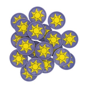 Puede incluir: Una colecci&oacute;n de fichas circulares moradas y amarillas. Cada ficha presenta un dise&ntilde;o de sol amarillo en el centro, rodeado por un borde morado. Las fichas est&aacute;n dispersas sobre un fondo blanco.