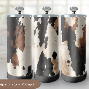 May include: Three black, brown, and white cowhide patterned bathroom tissue holders with silver tops and black bases.